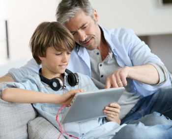 Boy and man sitting on the couch watching a tablet.