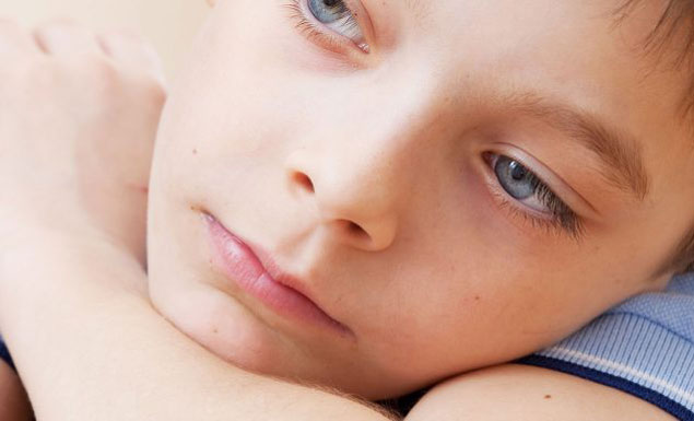 Young boy sitting with his head on his arms.